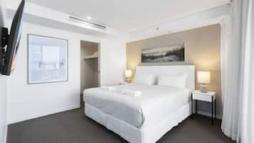 A hotel room with a bed, two bedside lamps, a TV mounted on the wall, a painting above the bed, and a door leading to a closet.