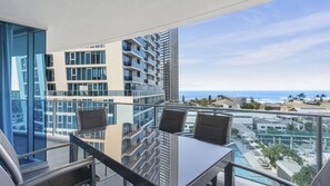 A balcony with a glass table and chairs, overlooking a cityscape and the ocean. - Orchid Residences Apartment 10704 (Surfers Paradise)