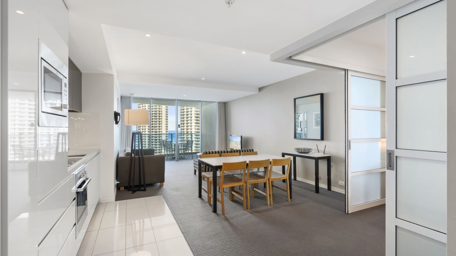 A modern kitchen with a dining area, large windows, and a view of high-rise buildings.
