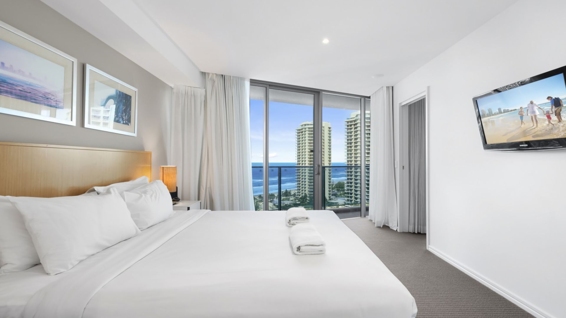 Ein Hotelzimmer mit einem großen Bett, einem Fernseher und einem Balkon mit Blick auf die Stadt.