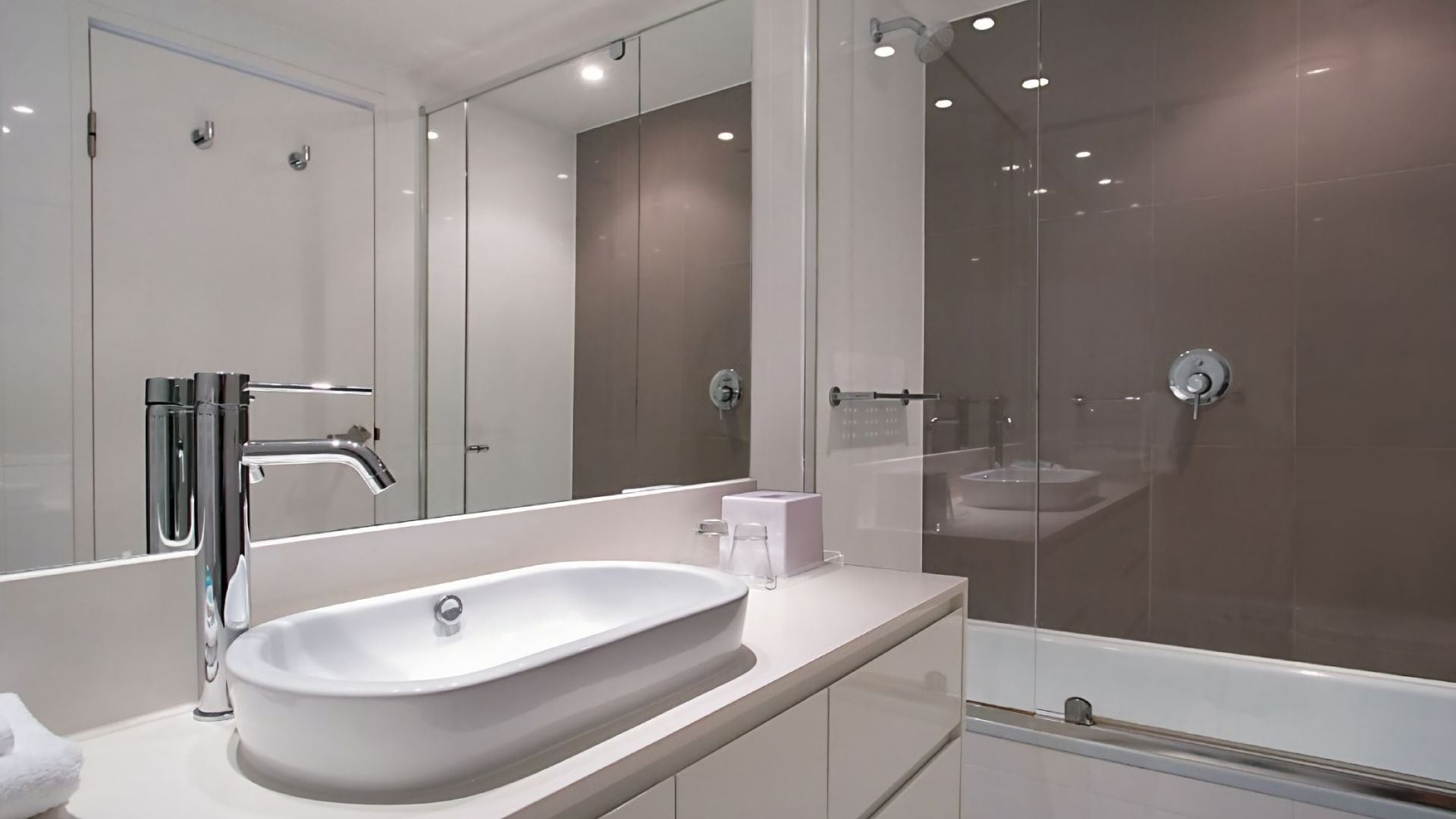 A modern bathroom with a large mirror, a white sink, and a glass-enclosed shower area.