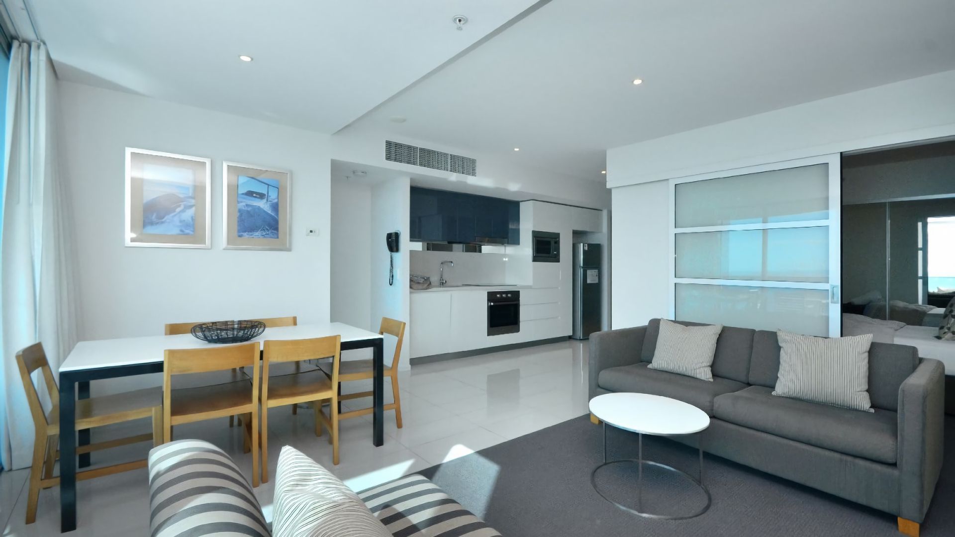 A modern living room with a sofa, a dining table with chairs, and a kitchen in the background.