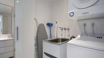 A modern bathroom with a built-in washing machine, a sink, and a shower area.