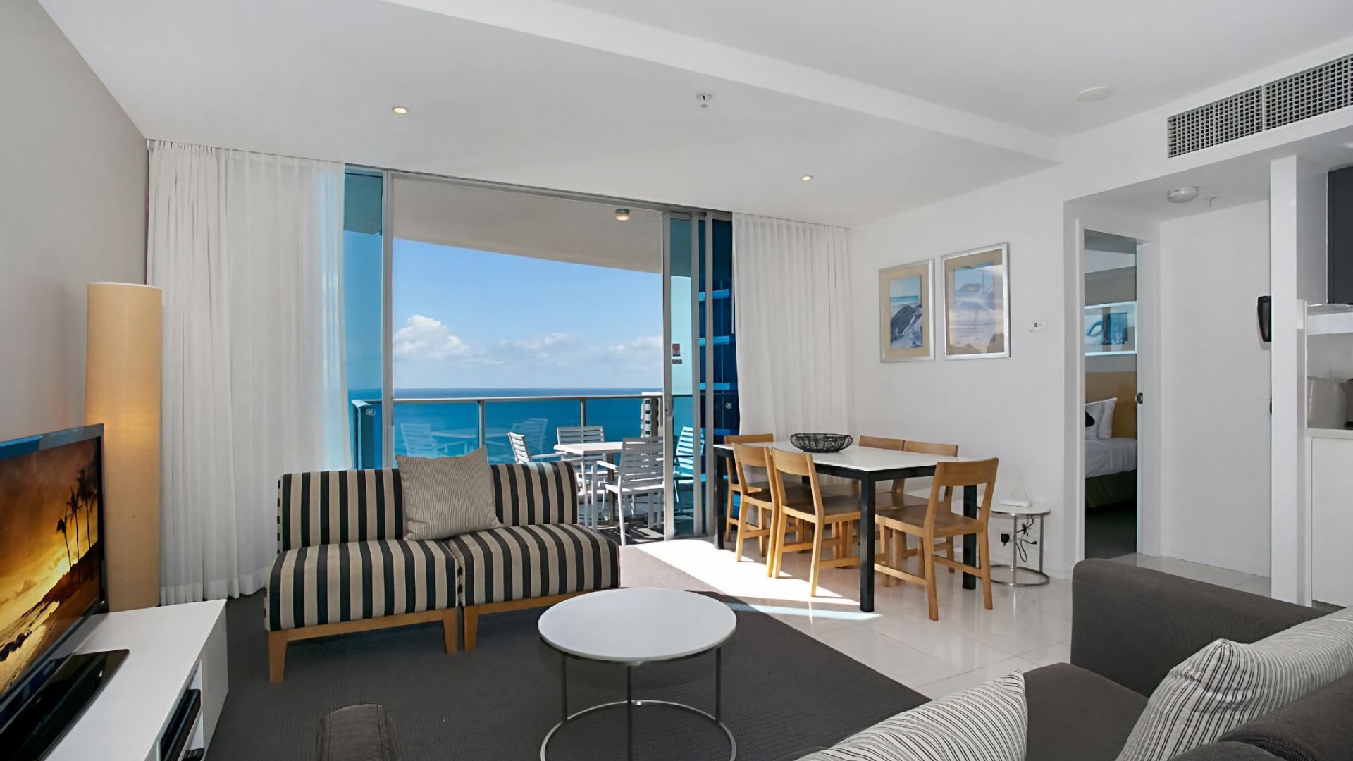 A modern hotel room with a balcony, a dining area, and a seating area with a TV.