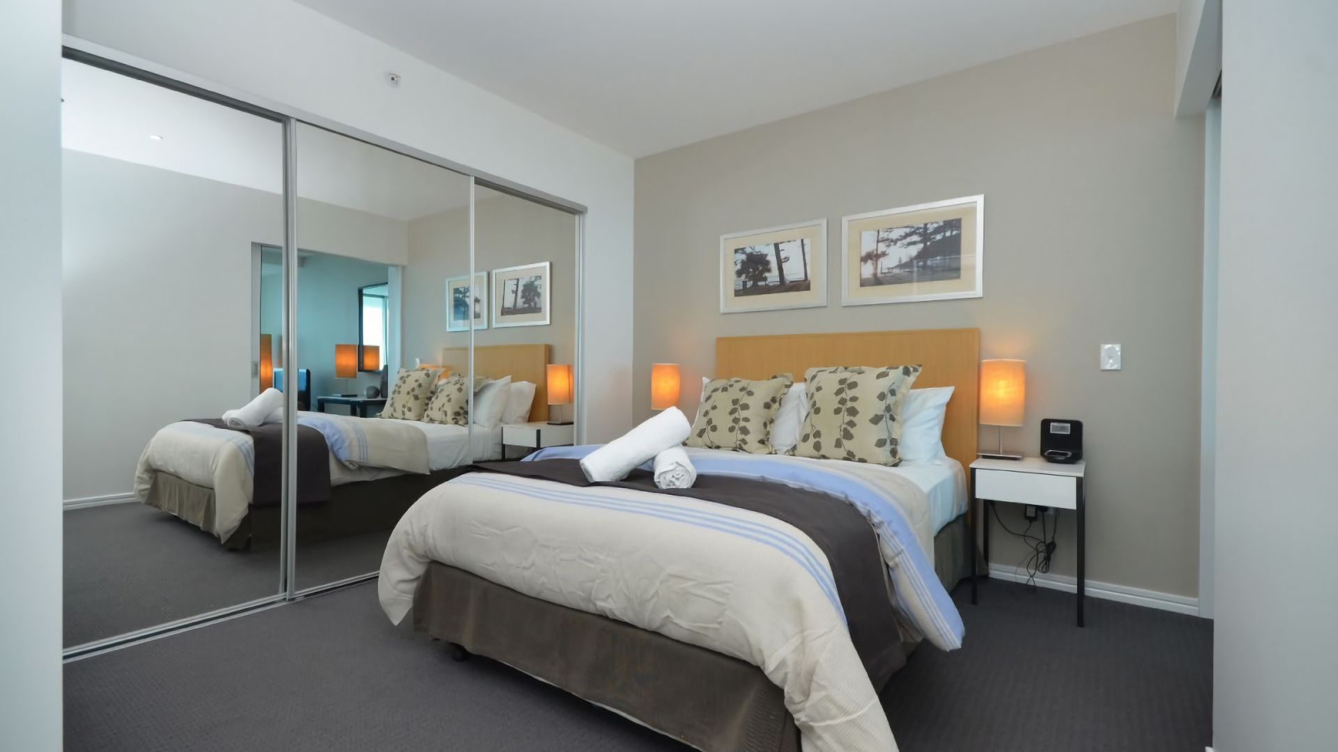 A hotel room with two beds, a large mirror, bedside lamps, and framed pictures on the wall.