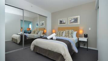 A hotel room with two beds, a large mirror, bedside lamps, and framed pictures on the wall.