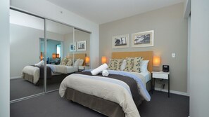 A hotel room with two beds, a large mirror, bedside lamps, and framed pictures on the wall. - Orchid Residences Apartment 12102 (Surfers Paradise)