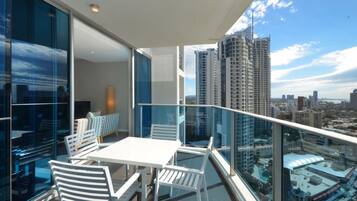 A balcony with a table and chairs, overlooking a cityscape with high-rise buildings.