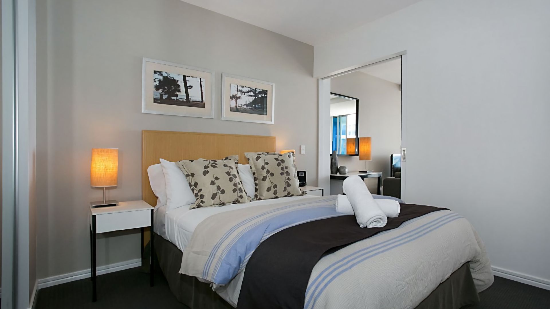 A hotel room with a bed, bedside tables, a lamp, and two framed pictures on the wall.