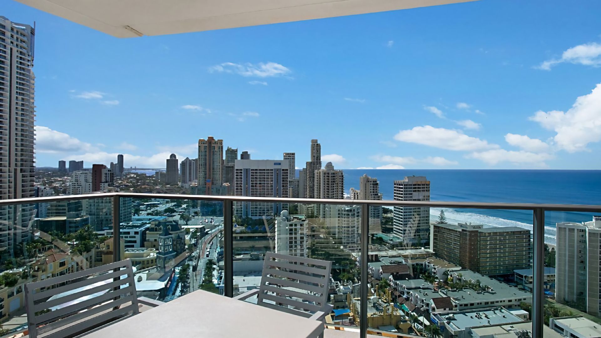 A balcony with a cityscape view, including high-rise buildings and a coastline.