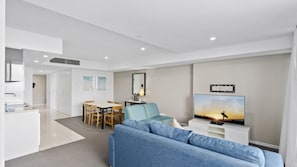 A modern living room with a sofa, TV, and dining area. - Orchid Residences Apartment 12105 (Surfers Paradise)