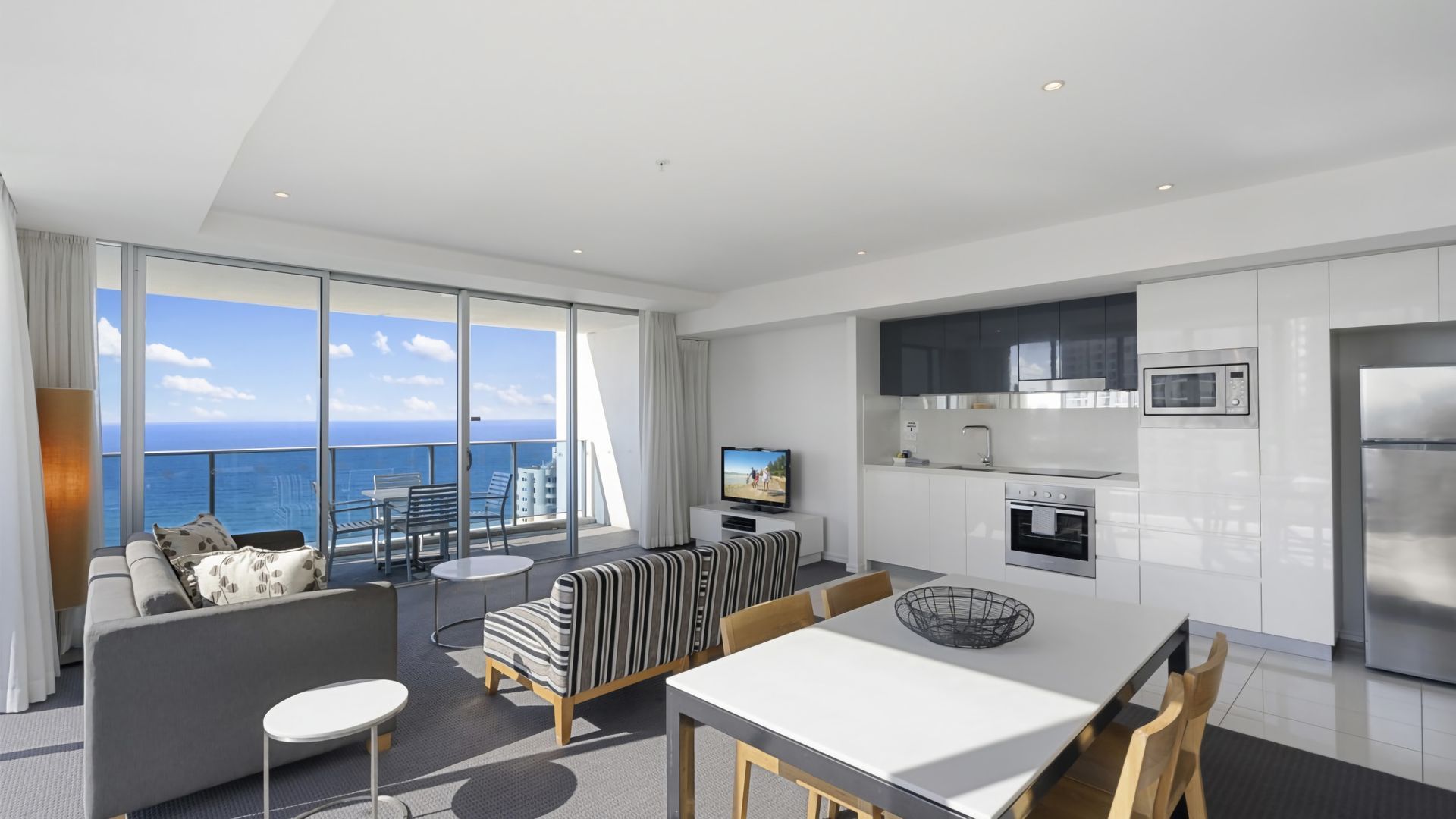 A modern living room with a balcony, a dining area, and a kitchen with stainless steel appliances.