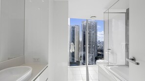 A modern bathroom with a bathtub, a glass shower enclosure, and a view of tall buildings. - Orchid Residences Apartment 12501 (Surfers Paradise)