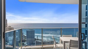 Een balkon met glazen hekwerk, met uitzicht op een stadsbeeld en de oceaan.
