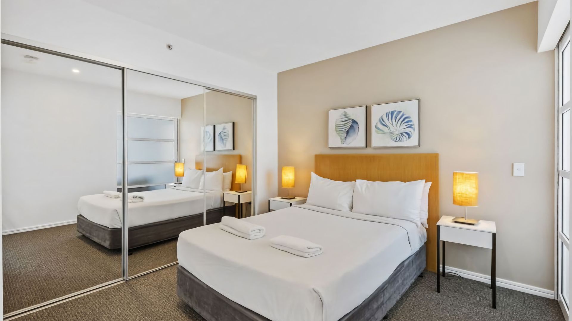 A hotel room with a large bed, bedside tables, a mirror, and artwork on the wall.