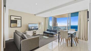 A modern hotel room with a balcony, a flat-screen TV, a sofa, a dining table, and a city view.