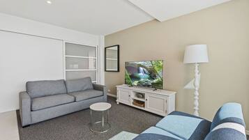 A modern living room with a grey sofa, a small round table, a TV on a white cabinet, and a lamp.