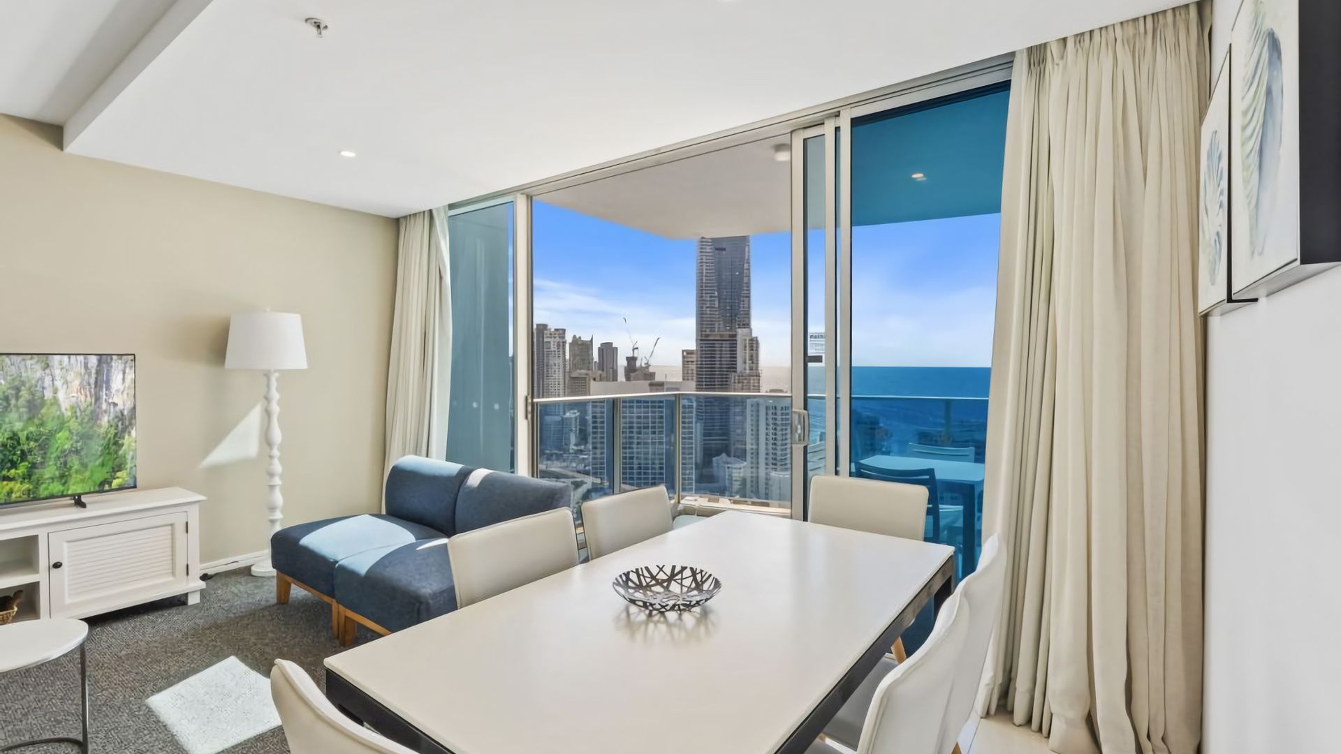 A hotel room with a balcony, a dining table, a sofa, and a TV.