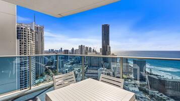A balcony with a table and chairs, overlooking a cityscape with high-rise buildings and a view of the ocean.