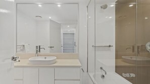 A modern bathroom with a large mirror, a sink, and a shower area. - Orchid Residences Apartment 12702 (Surfers Paradise)