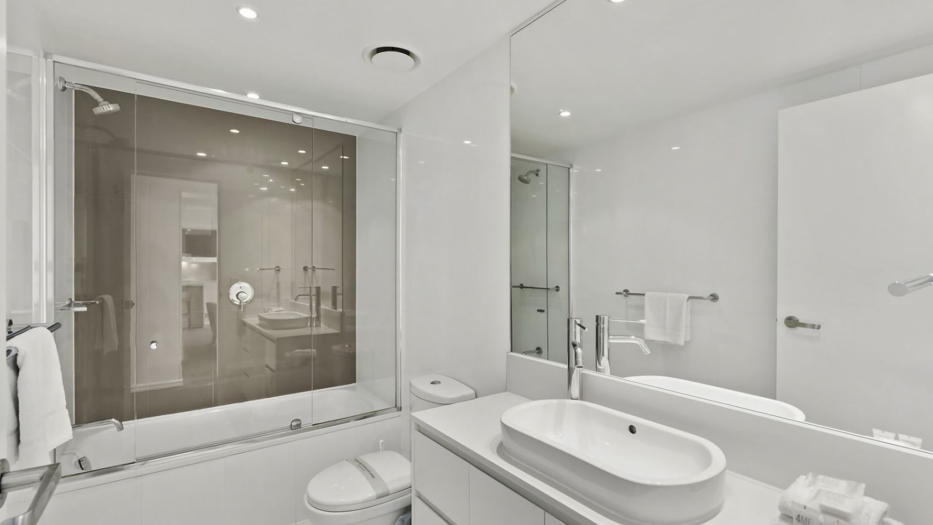 A modern bathroom with a glass-enclosed shower, a freestanding bathtub, a vanity with a large sink, and a toilet.