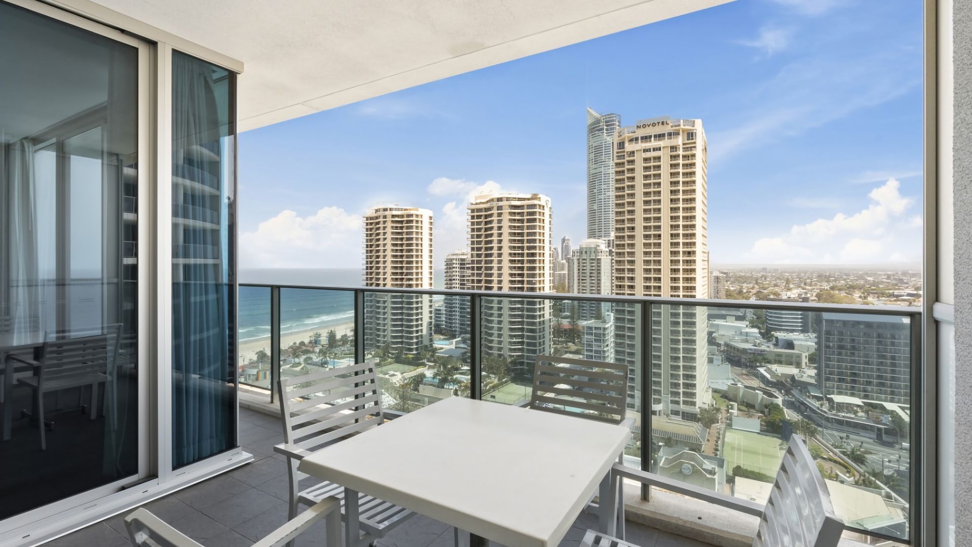 A balcony with a table and chairs, overlooking a cityscape with high-rise buildings and a beach.