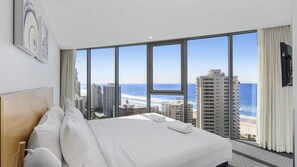 A hotel room with a large bed, a view of the beach, and a cityscape. - Orchid Residences Apartment 21803 (Surfers Paradise)