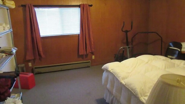 Una habitación con cama, ventana con cortinas, radiador y una silla.