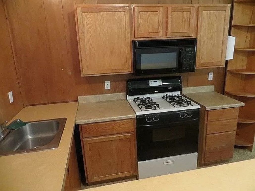 A kitchen with wooden cabinets, a microwave, a gas stove, and a sink.