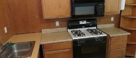 A kitchen with wooden cabinets, a microwave, a gas stove, and a sink.