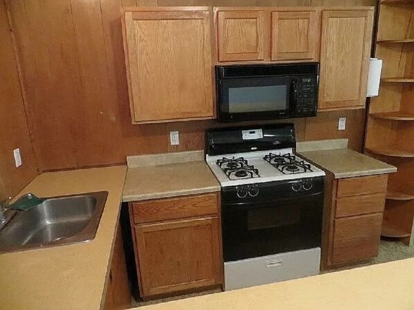 Una cocina con armarios de madera, un microondas, una estufa a gas y un lavabo.