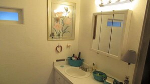 Un baño con lavamanos, espejo y una obra de arte floral enmarcada en la pared.