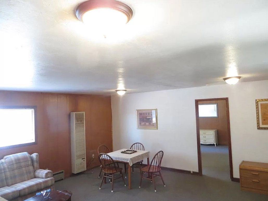 A room with a dining table, chairs, a sofa, a heater, and a small cabinet.