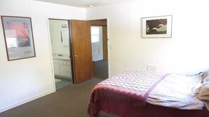 Un dormitorio con cama, una puerta que da a un baño y un cuadro en la pared.
