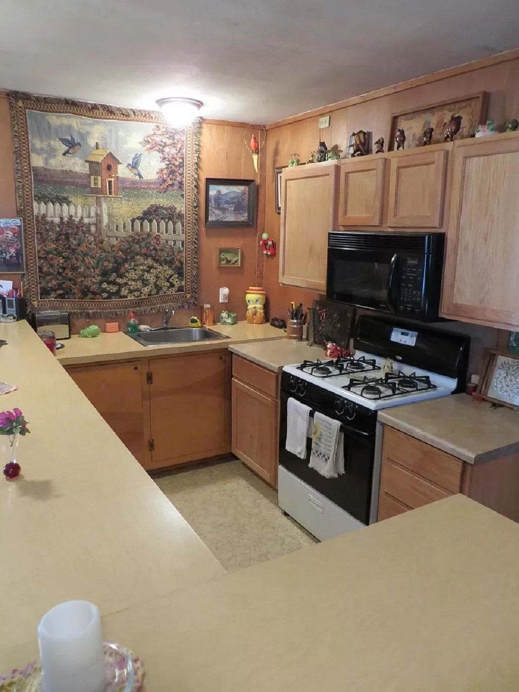 Une cuisine avec des meubles de rangement en bois, une cuisinière à gaz, un four à micro-ondes et un tableau accroché au mur.