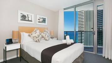 A hotel room with a bed, bedside tables, a laptop, and a view of the ocean through a balcony with a glass door.
