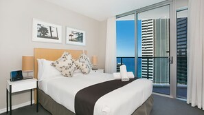 Quarto de hotel com cama, mesas de cabeceira, um laptop e vista para o oceano através de varanda com porta de vidro.