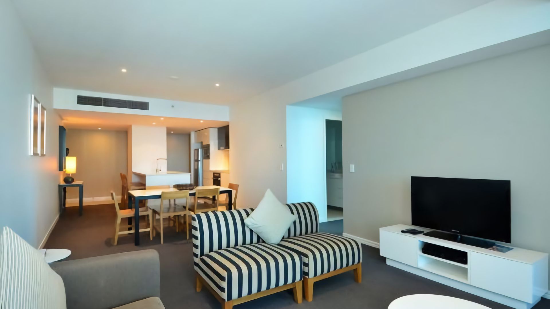 Una sala de estar moderna con un sofá, una televisión y un comedor con sillas y una mesa.
