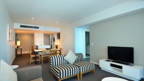 A modern living room with a sofa, a television, and a dining area with chairs and a table. - Orchid Residences Apartment 22303 (Surfers Paradise)