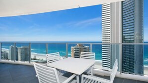 A balcony with a table and chairs, overlooking a beach and cityscape. - Orchid Residences Apartment 22303 (Surfers Paradise)