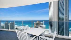 Varanda com mesa e cadeiras, vista para a praia e o horizonte urbano.