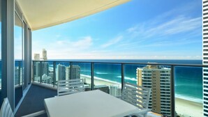 A balcony with a table and chairs, overlooking a beach and ocean with high-rise buildings in the background. - Orchid Residences Apartment 22303 (Surfers Paradise)