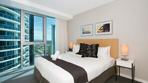 A hotel room with a large bed, two bedside tables, a view of the cityscape through floor-to-ceiling windows, and two framed artworks on the wall. - Orchid Residences Apartment 22306 (Surfers Paradise)
