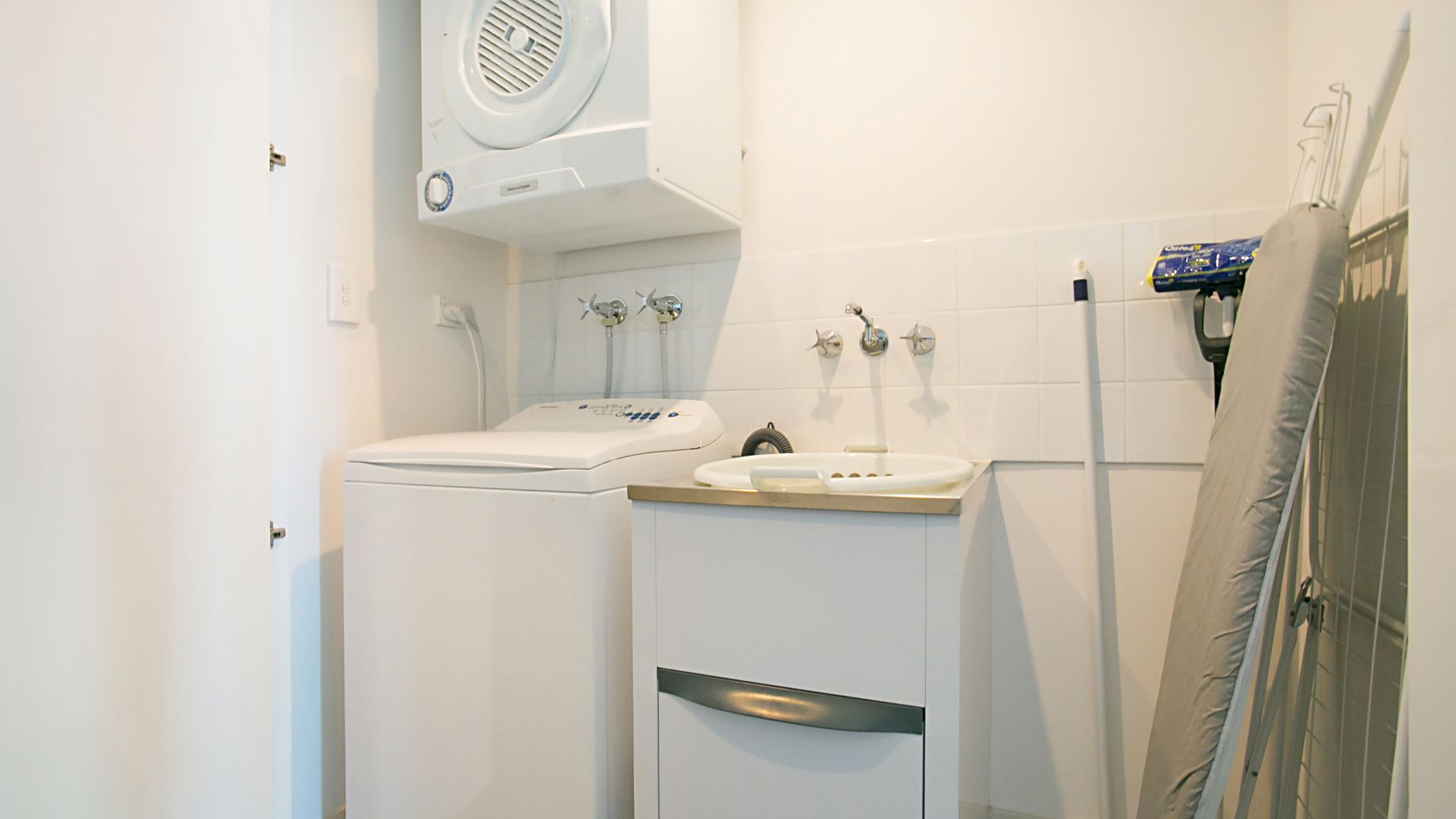 A compact bathroom with a washing machine, a sink, and a shower.