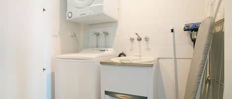 A compact bathroom with a washing machine, a sink, and a shower.