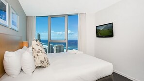 A hotel room with a large bed, a flat-screen TV, and a view of the ocean and cityscape through floor-to-ceiling windows. - Orchid Residences Apartment 22402 (Surfers Paradise)