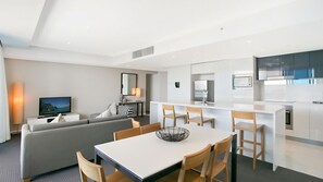 A modern living room with a sofa, a dining table with chairs, a TV, and a kitchen area with a microwave and cabinets. - Orchid Residences Apartment 22402 (Surfers Paradise)