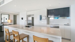 A modern kitchen with a central island, bar stools, and stainless steel appliances. - Orchid Residences Apartment 22402 (Surfers Paradise)