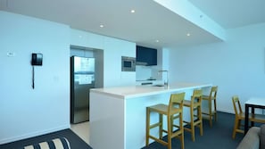 A modern kitchen with a central island, bar stools, and a dining area with a table and chairs. - Orchid Residences Apartment 22402 (Surfers Paradise)