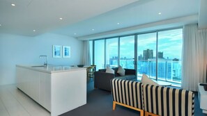 A modern living room with a sofa, a striped armchair, and a kitchen area with a white countertop. - Orchid Residences Apartment 22402 (Surfers Paradise)